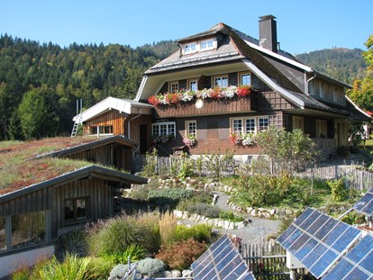Naturhotel - Preisklasse: € - Baden-Württemberg - Haus Sonne im Sommer, im Vordergrund der Kräutergarten und Solarpanels. - Haus Sonne - das vegetarische Bio-Hotel